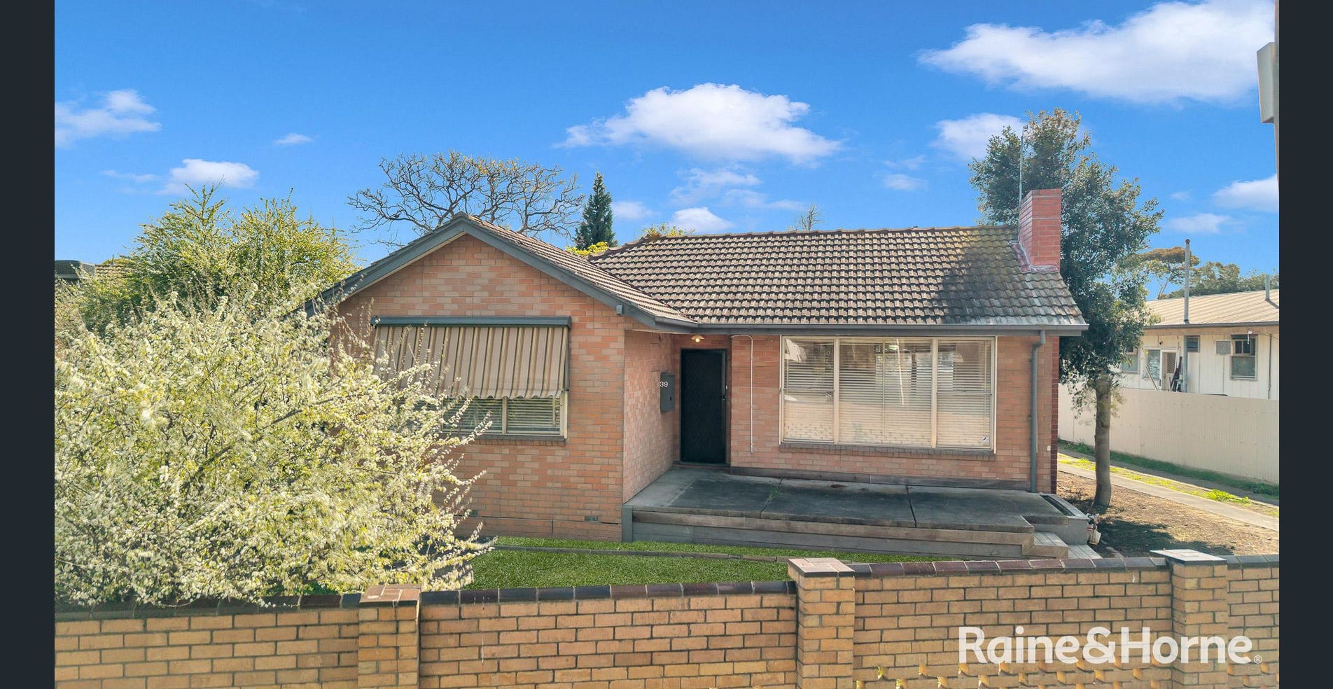 39 Bacchus Marsh Road, Corio, VIC. A single-storey exposed-brick house with a tiled roof, brick chimney, broad front windows and a front garden.